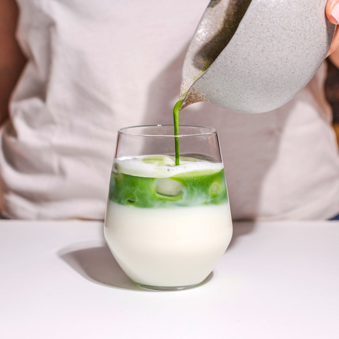 Pouring vibrant green DAKYS matcha over iced milk to create a refreshing iced matcha latte. A clean energy drink packed with L-theanine for calm focus, sustained energy, and a smooth taste — perfect for hot days and productive afternoons.