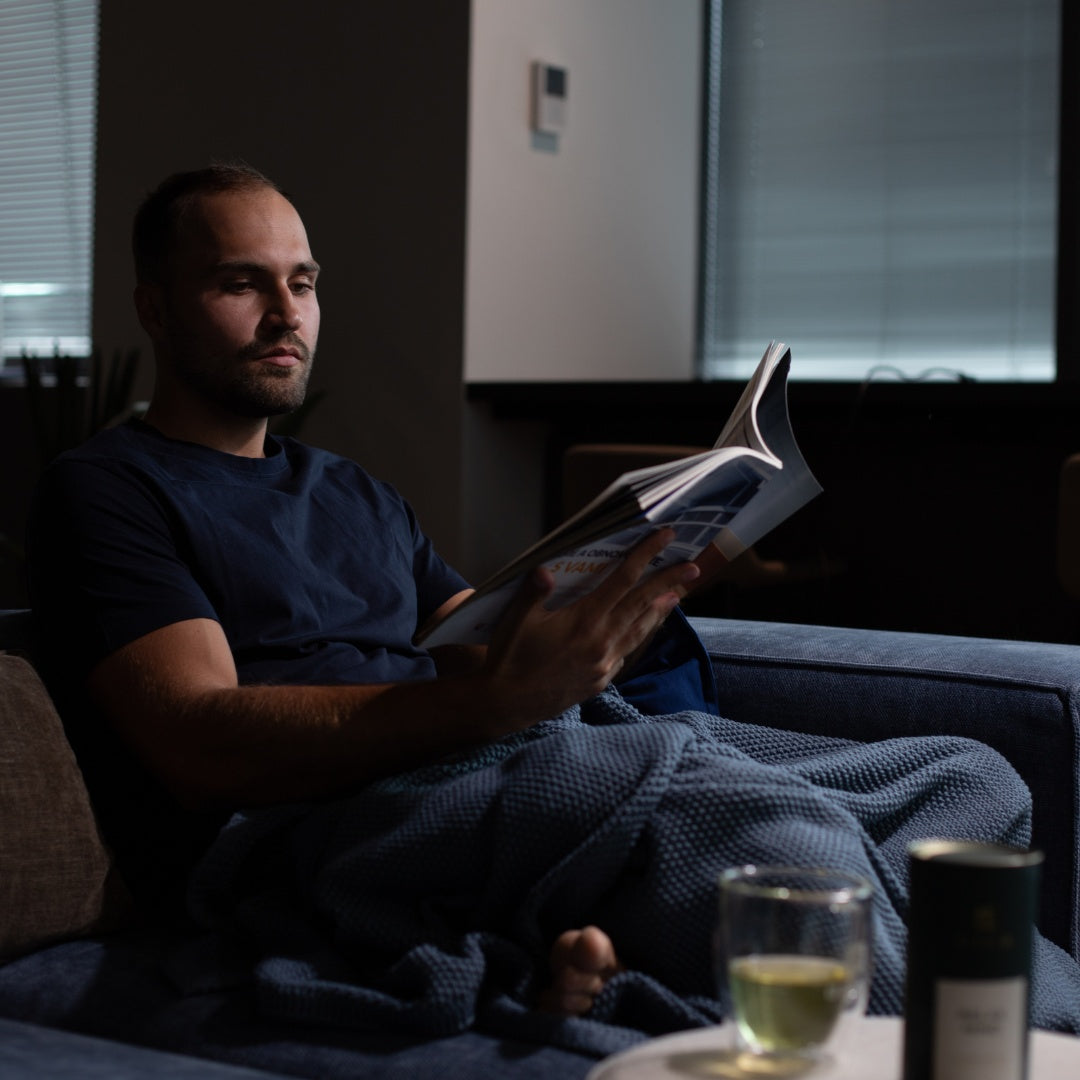Man relaxing on a couch with a book and a cup of Dakys recovery drink – promoting evening calm, deep rest, and ultra-clean regeneration.